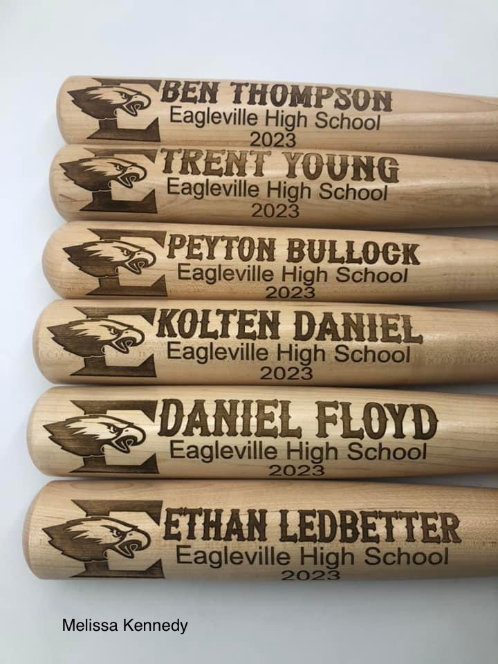 A set of custom laser-engraved wooden baseball bats featuring player names, school names, graduation years, and a detailed school logo, creating a personalized and memorable keepsake.
